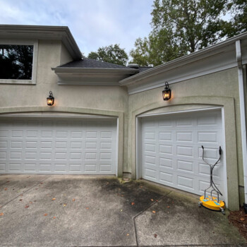 Two closed garage doors on a stucco house, with a yellow pressure washer leaning against the right door.