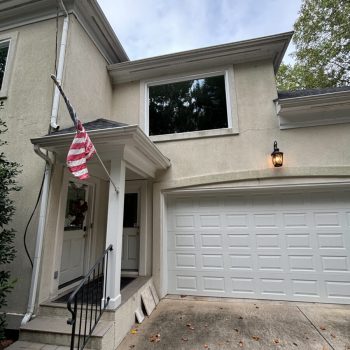Two-story house with a garage, an American flag, and a lit porch light on a cloudy day.